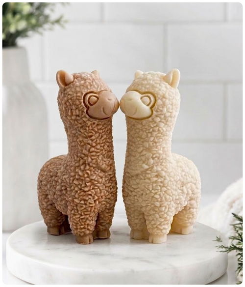 Two alpaca vegan soaps standing side by side on a rectangular stone base, photographed in a softly lit indoor setting.