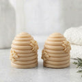 Two soft yellow coloured soaps shaped like beehives, shown side by side on a light grey surface with a soft, blurred background.