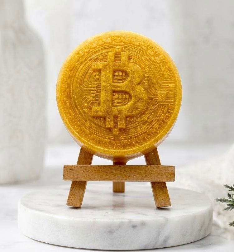 A large, gold circular vegan soap bar, in the shape of a golden Bitcoin, supported upright on a miniature wooden easel.