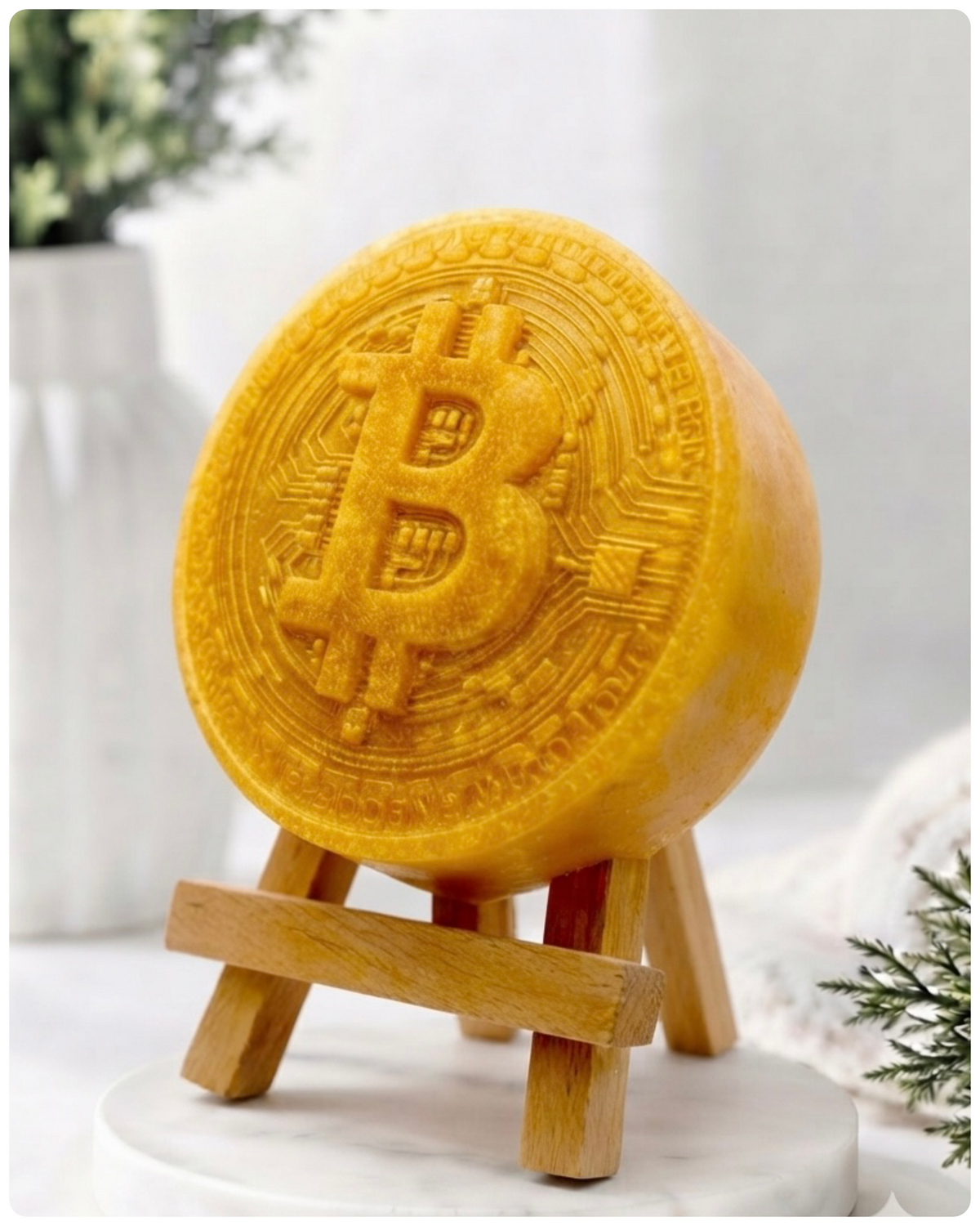 handmade vegan soap in the shape of a Bitcoin coin with a shimmering glitter finish, featuring a detailed relief of the "B" symbol and circuit board patterns, displayed on a small wooden easel in a bright farmhouse decor setting.