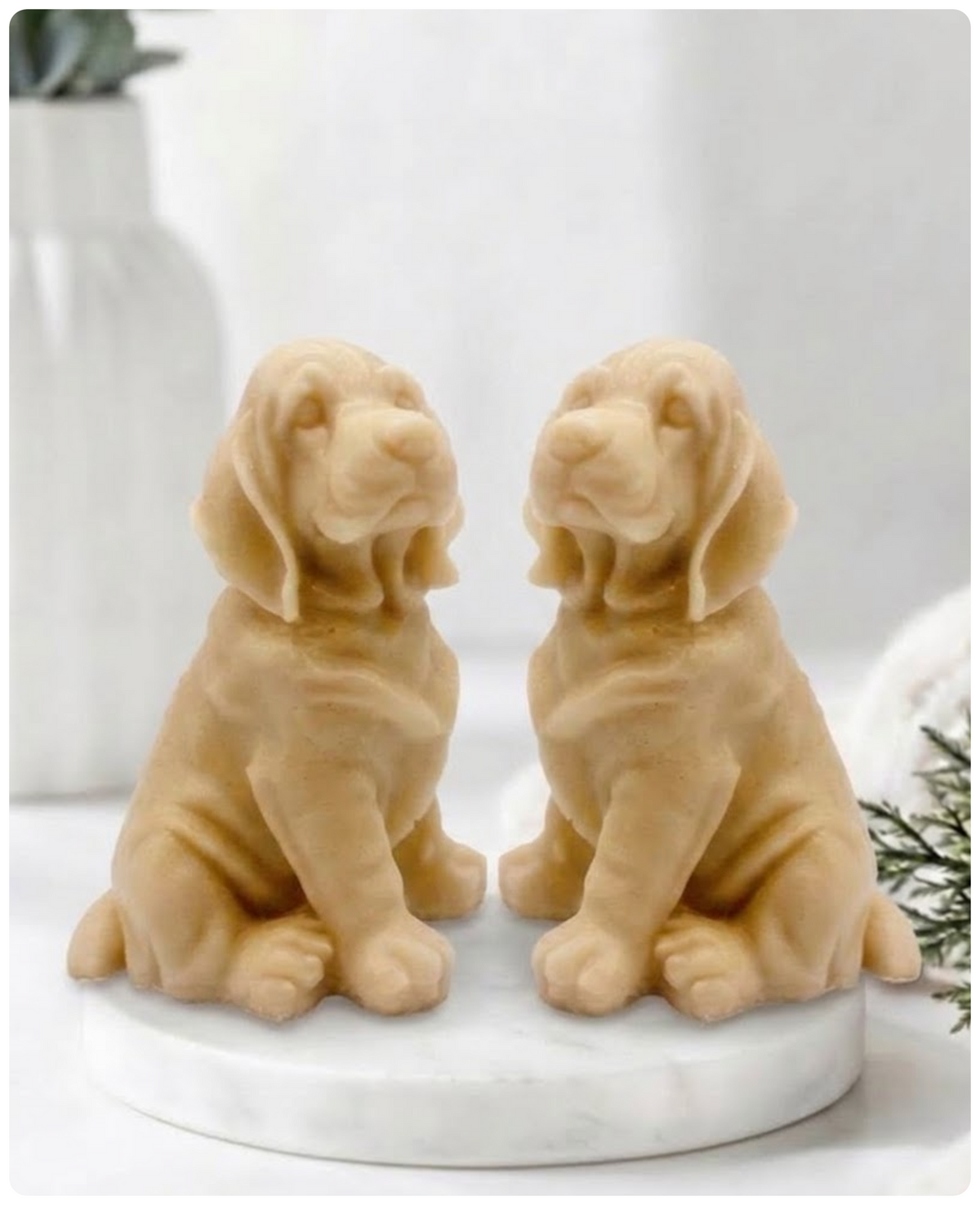 Two yellow French clay bloodhound soaps sitting on a white marble display stand with a soft bathroom background.