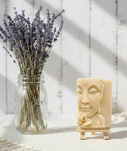 Load image into Gallery viewer, handmade vegan soap featuring a detailed 3D relief of a serene Buddha face with a lotus flower, displayed on a wooden easel against a whimsical farmhouse decor background.
