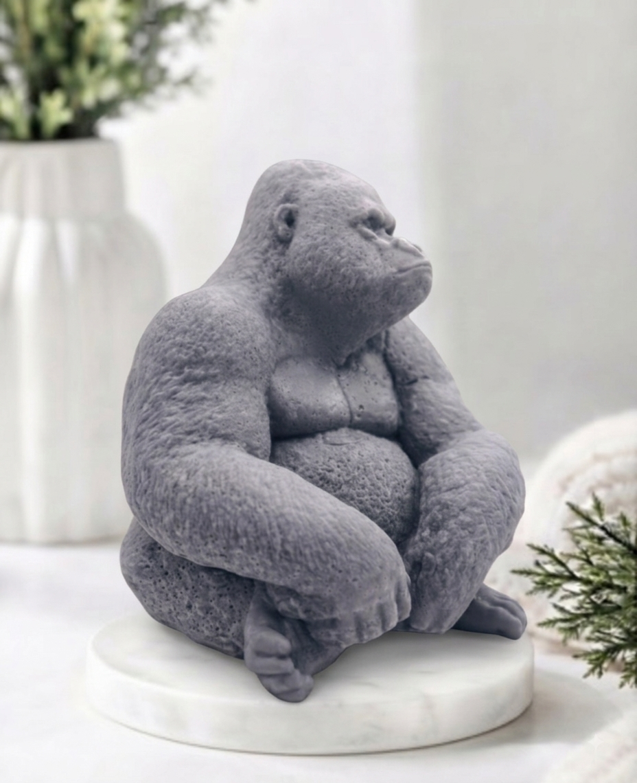 A large gray gorilla handmade soap sitting on a white marble base, photographed in a softly styled indoor setting with blurred decor in the background.