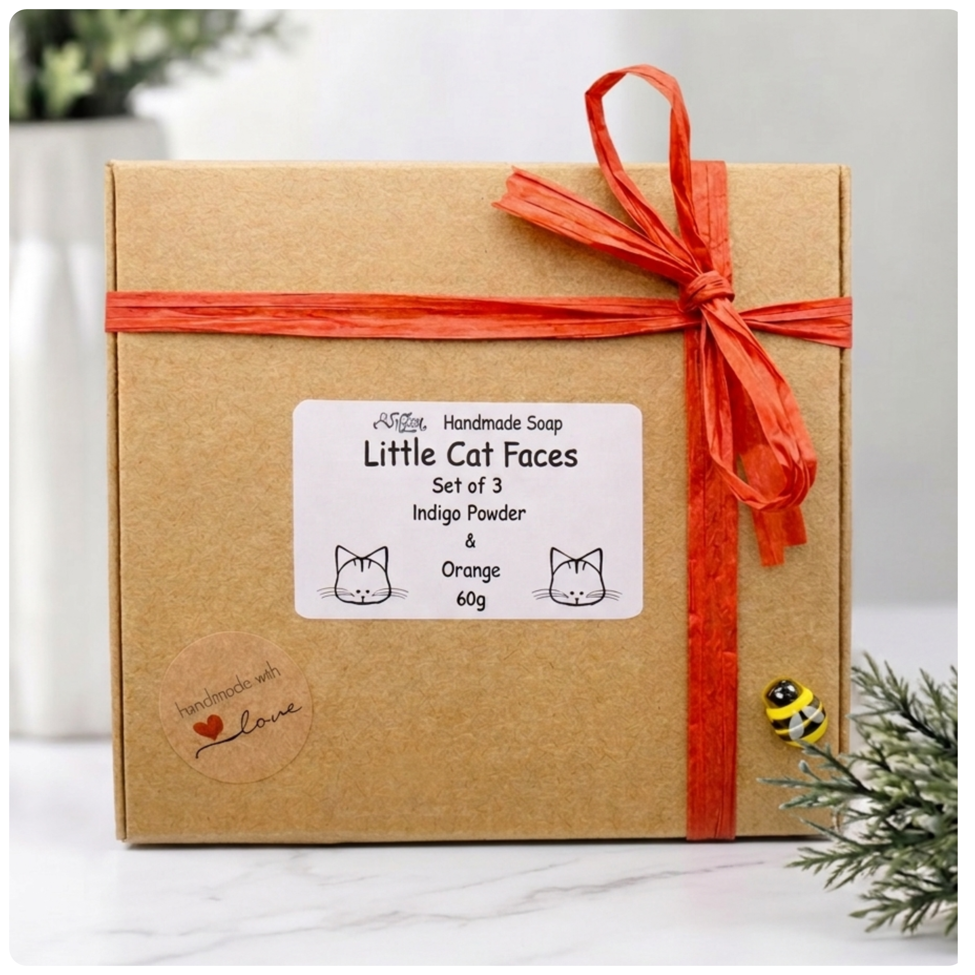 Three dark grey handmade cat face soaps featuring round eyes, chubby cheeks, and detailed fur texture stacked on a small wooden display easel on a marble coaster.