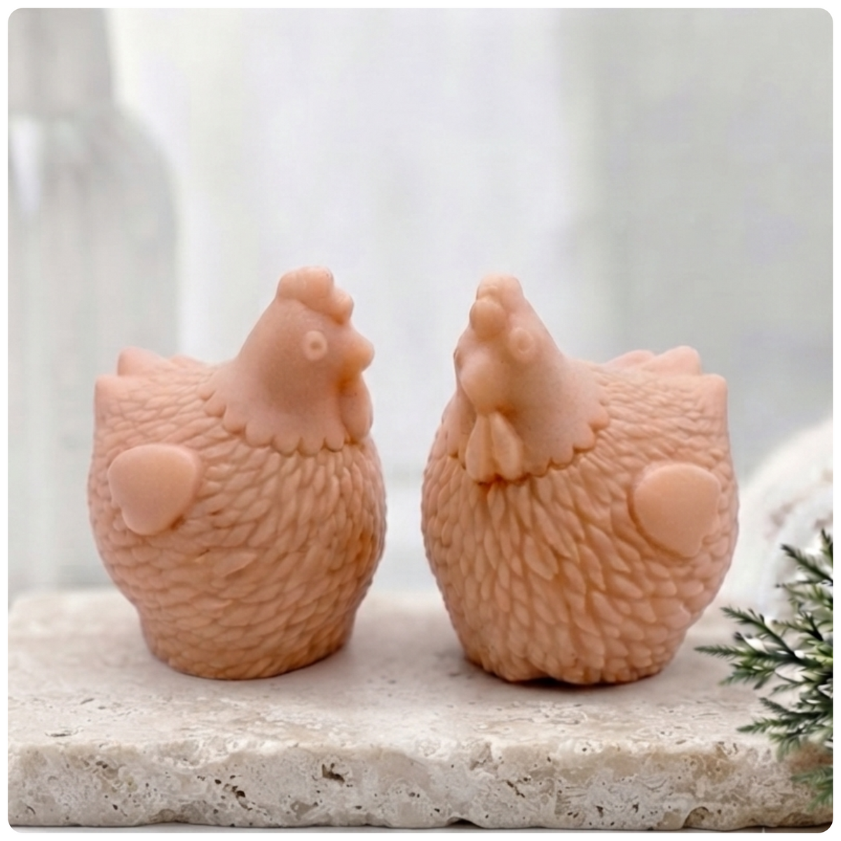 Two handmade vegan soaps in the shape of plump, realistic chicken sculptures with detailed feather textures, displayed on a rustic white wooden surface in a bright farmhouse decor setting.