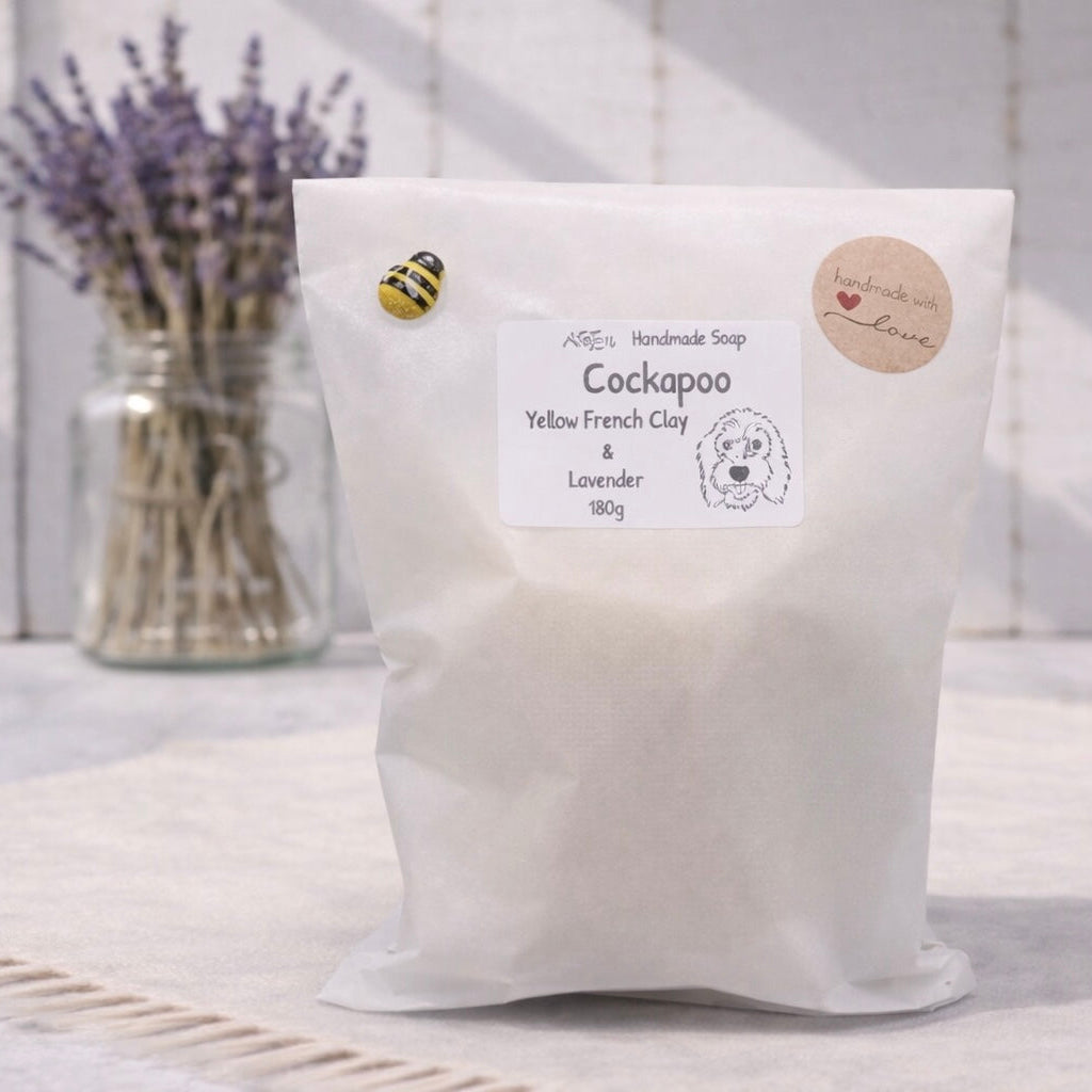 Bag of Cockapoo Yellow French Clay & Lavender soap with a jar of lavender flowers in the background.