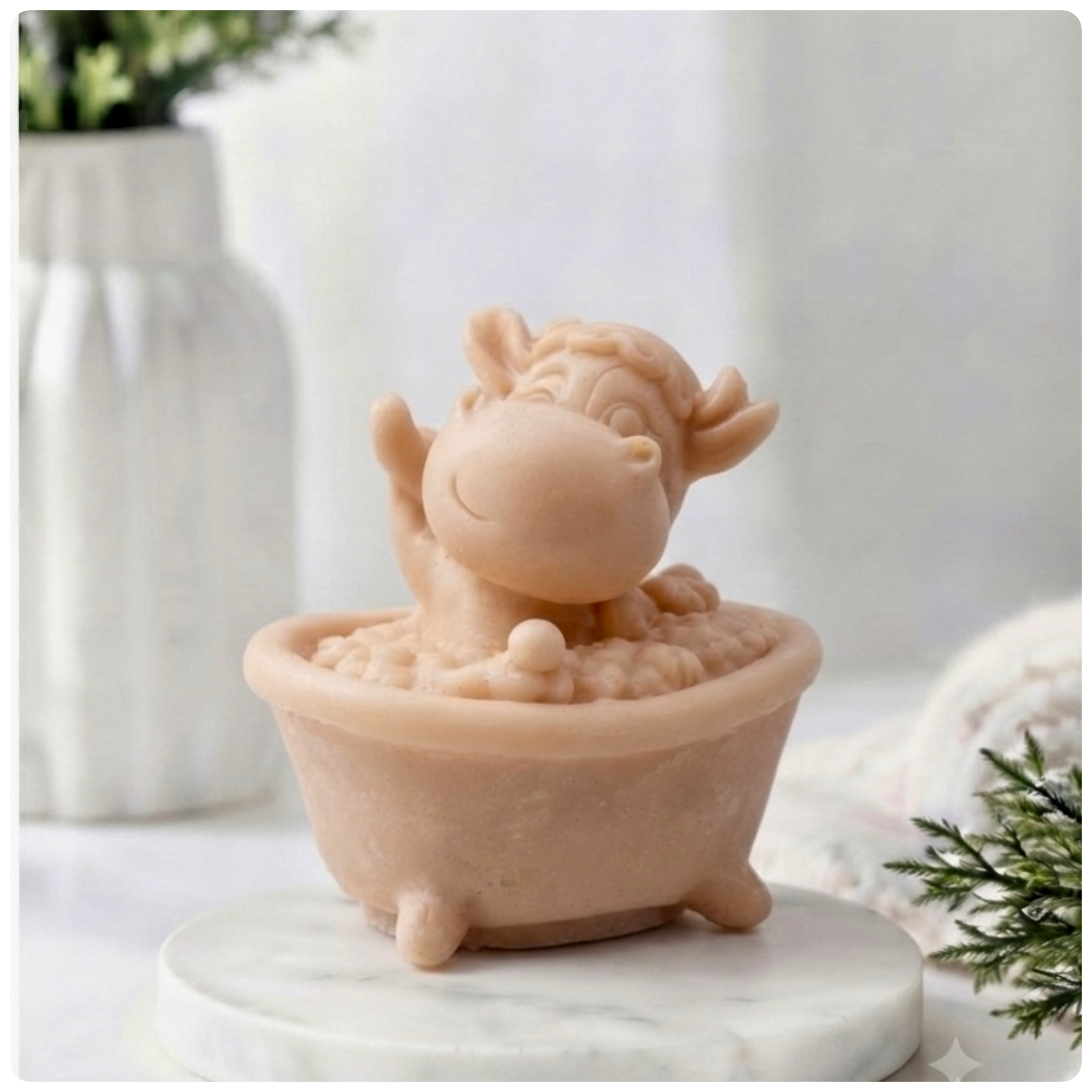 A handmade vegan soap gift sculpted in the shape of a "dirty cow" character happily sitting in a bubble-filled roll-top bathtub with one hoof raised, displayed on a light wooden surface.