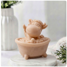 Load image into Gallery viewer, A handmade vegan soap gift sculpted in the shape of a "dirty cow" character happily sitting in a bubble-filled roll-top bathtub with one hoof raised, displayed on a light wooden surface.
