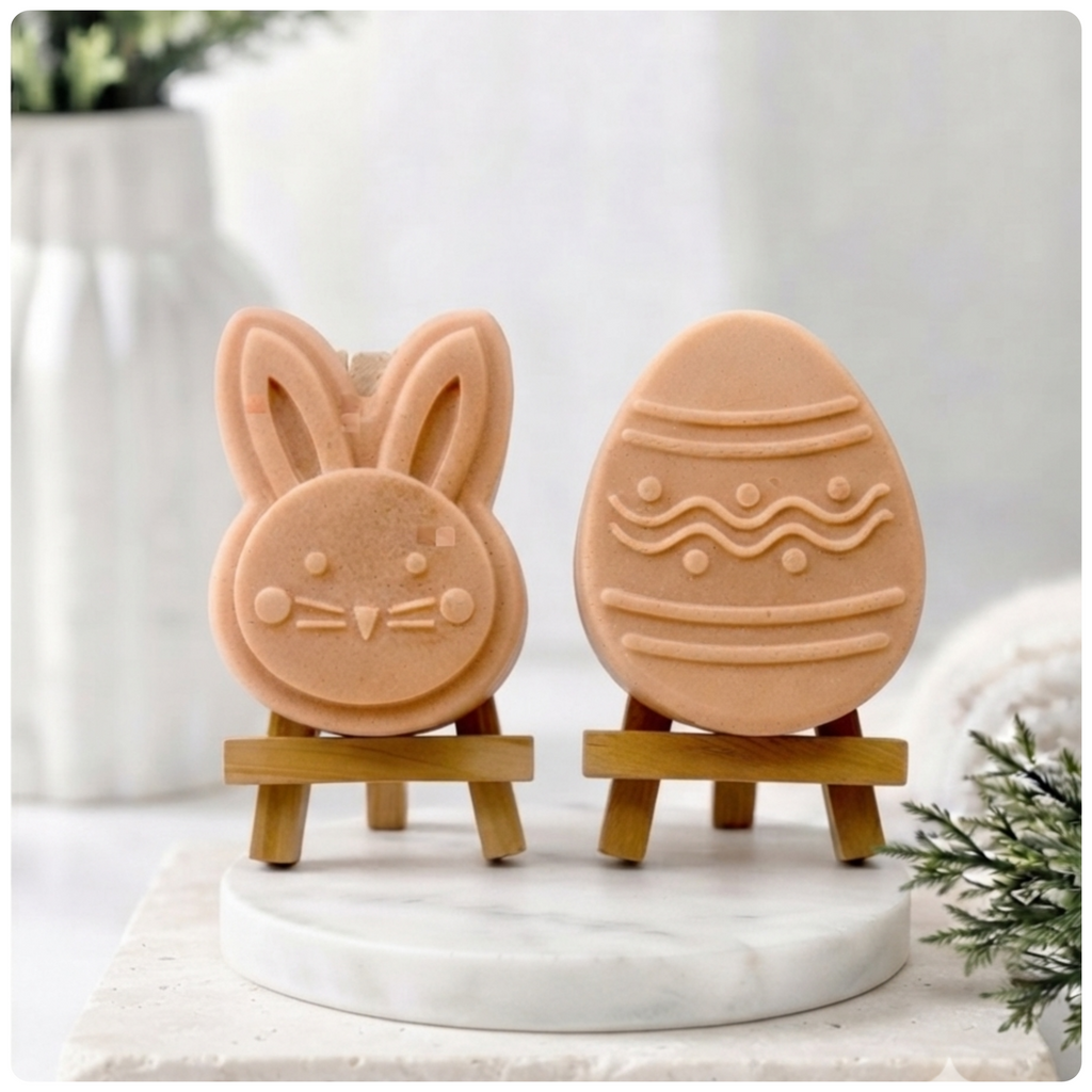 handmade vegan soap gift set featuring a cute bunny face and a decorated Easter egg with wave patterns, displayed on wooden easels against a rustic white farmhouse decor background with spring flowers.