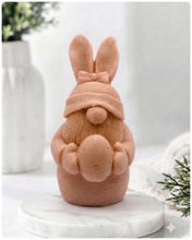 Load image into Gallery viewer, A detailed handmade vegan soap in a natural colour, sculpted as a whimsical Easter gnome (gonk) with long rabbit ears and a bow on its hat, holding a patterned Easter egg, displayed on a light wooden surface. Easter gift 
