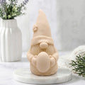 A detailed soft yellow handmade vegan soap gift,  sculpted as a whimsical Easter gnome (gonk) wearing a tall pointed hat with a flower detail, holding a large patterned Easter egg.