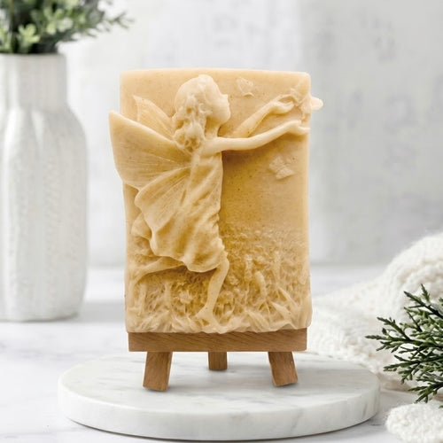Soft yellow coloured vegan fairy soap bar with a handcrafted artisan fairy and butterfly pattern, standing on a miniature wooden easel. Natural essential oil soap, unique self-care gift 