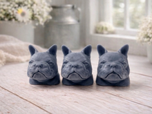 Load image into Gallery viewer, three french bulldog-head shaped bars of soap, side-by-side, on a wooden surface, set in a cosy, rustic bathroom with a vase of white and yellow flowers
