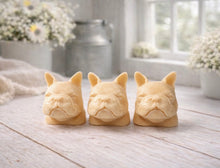 Load image into Gallery viewer, three french bulldog-head shaped bars of soap, side-by-side, on a wooden surface, set in a cozy, rustic bathroom with a vase of white and yellow flowers
