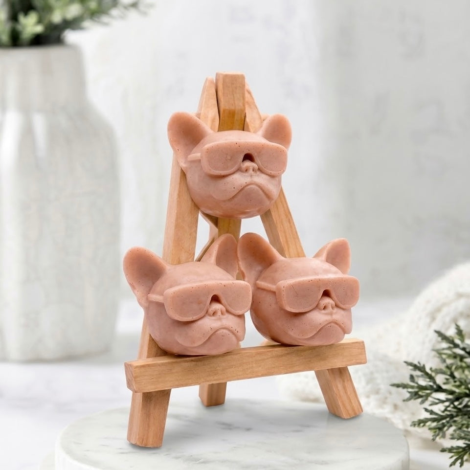 Handmade French Bulldog head soaps gift set. Three unique, detailed novelty soaps shaped as Frenchies in sunglasses are arranged in a stacking formation on a miniature wooden easel display. Made in a terracotta colour. 