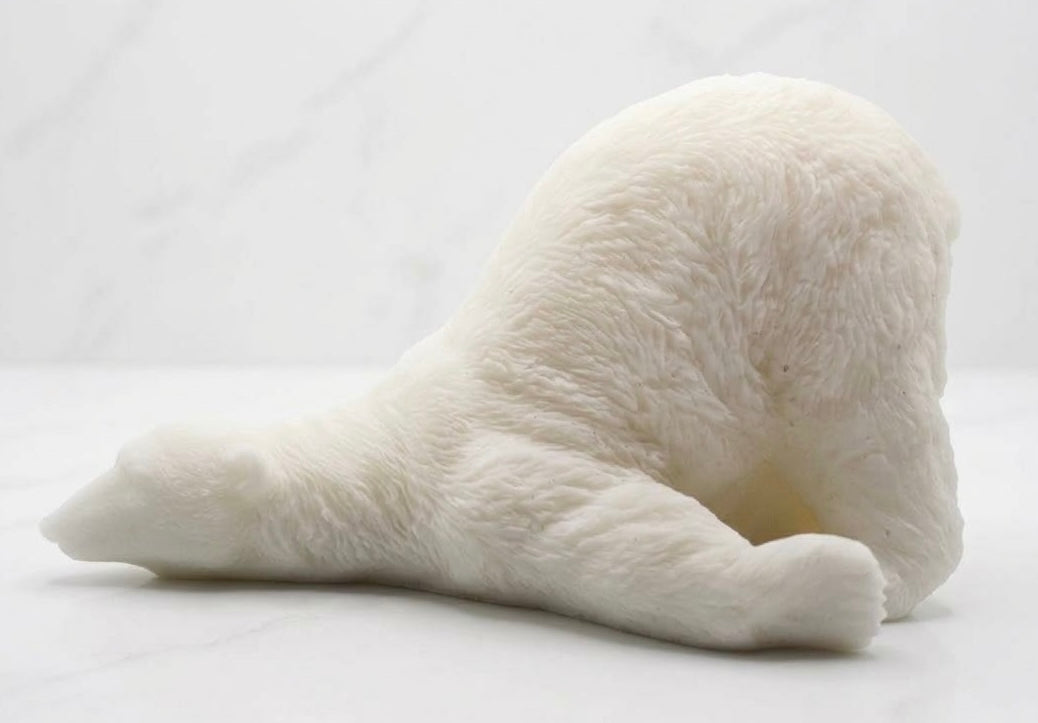 A pure white bar of soap intricately carved into the detailed shape of a lazy polar bear lying down on its side, on a white marble surface.