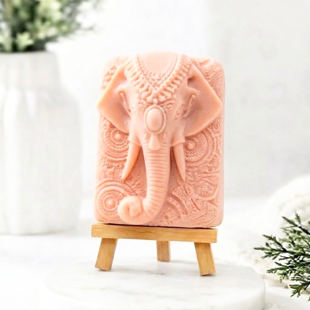 A bar of pink soap on a miniature wooden easel, displaying the detailed head-on carving of Ganesha's elephant head and elaborate patterned ears.