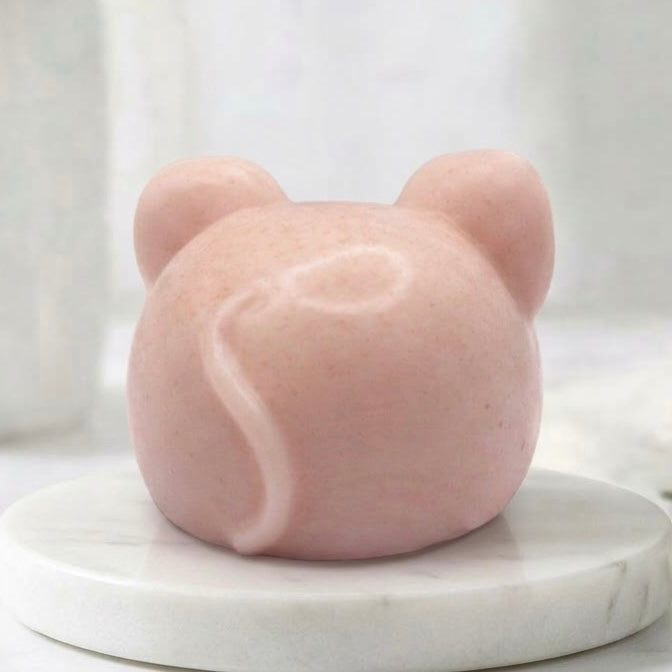 A rear view of a soft pink handmade vegan soap sculpted into the shape of a cute resting mouse with large rounded ears and a delicate snout