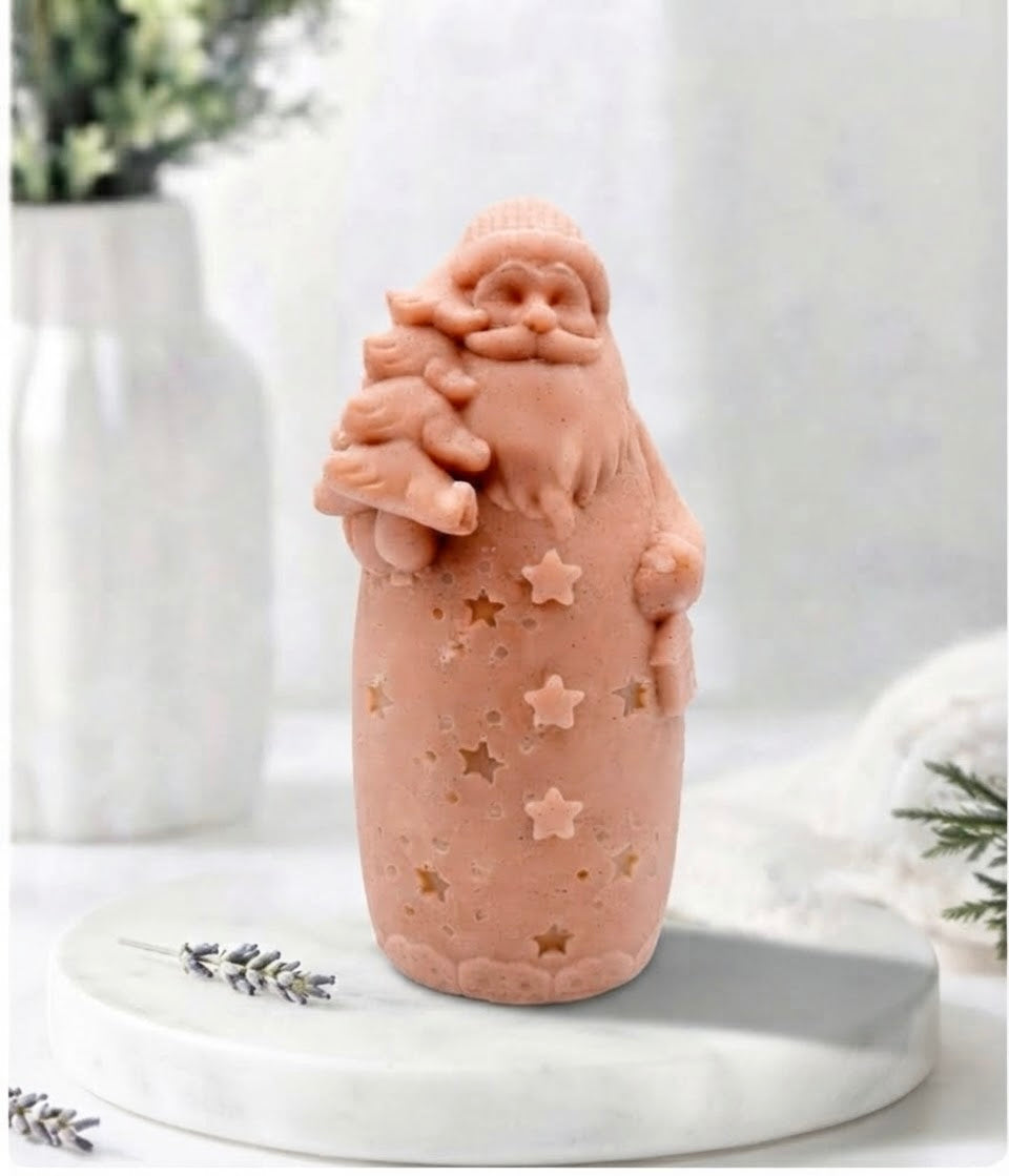 A red French clay Santa Claus soap shaped like him holding a Christmas tree, displayed on a white marble tray with a soft, blurred holiday background.