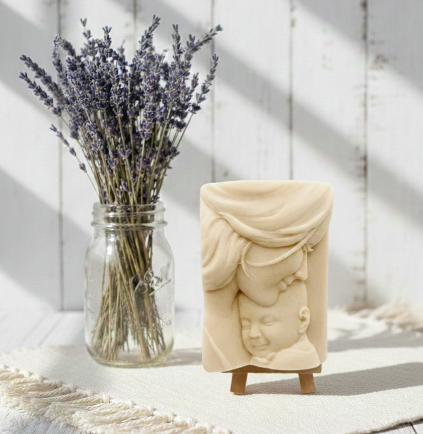 handmade vegan soap featuring a tender mother kissing her baby's forehead, displayed on a wooden easel against a whimsical farmhouse decor background.