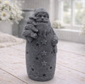 handmade vegan soap sculpted into a tall figure of Father Christmas wearing star-patterned robes, holding a small Christmas tree in one arm and a lantern in the other, set in a bright farmhouse window.