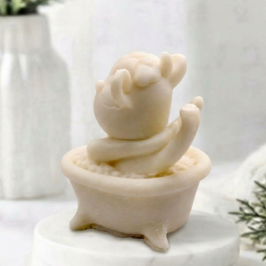 Rear view perspective of a soft yellow novelty vegan soap bar sculpted into a cartoon cow figure sitting inside a matching miniature footed bathtub.