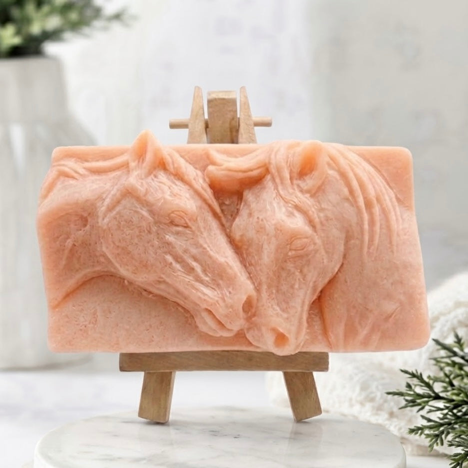 A detailed close-up image of a sculpted pink vegan and cruelty-free handmade soap bar, featuring a high-relief carving of a mare and foal horses nuzzling. The intricate design highlights the horse manes and facial features, making it a unique equestrian gift.