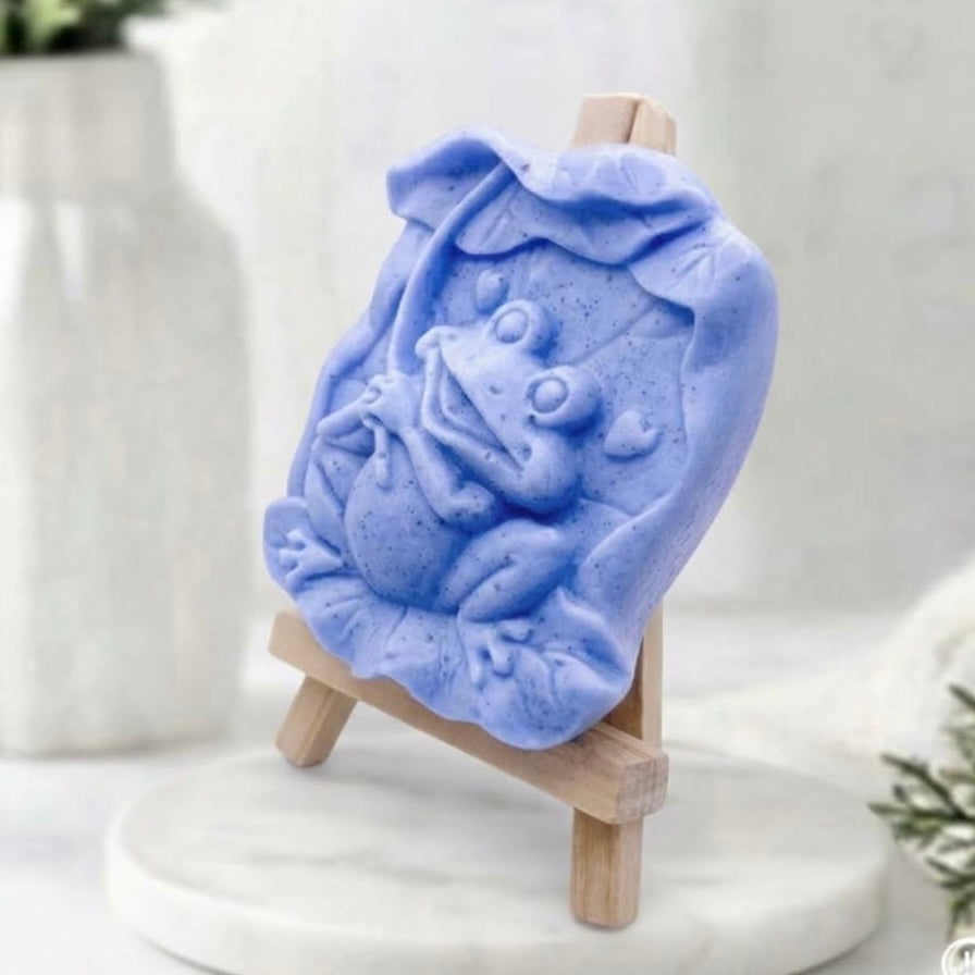 A side view of a cruelty-free vegan bar soap featuring a happy frog, made with natural indigo powder for a soft blue colour, perfect as a novelty animal soap gift.