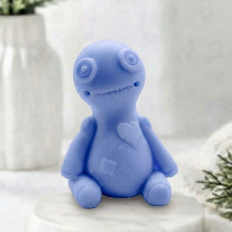 This soft blue voodoo doll soap is highly detailed, including spiral eyes, a stitched mouth, and carved heart and belly patches, against a bright, softly blurred bathroom background