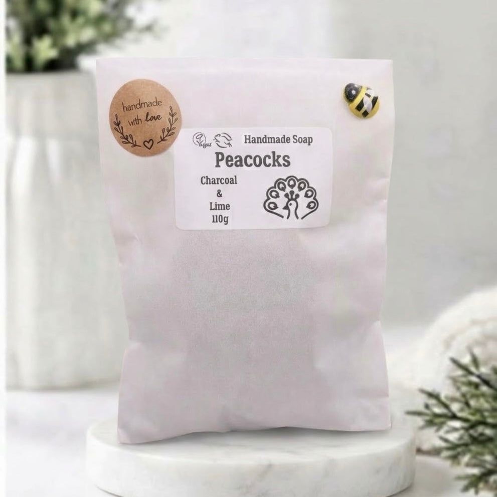 White pouch packaging for handmade charcoal and lime peacock soap, 110g, with a bee emblem and "handmade with love" label.
