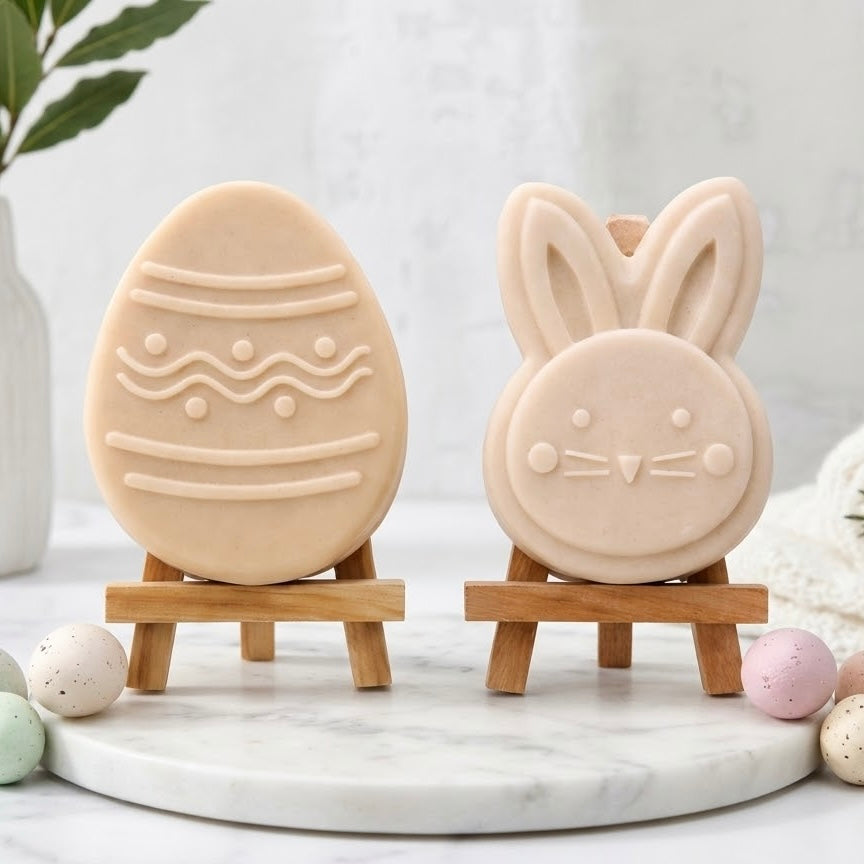 Neutral soft yellow coloured Easter soap gift set with two vegan soaps on mini wooden easels. Features a patterned off-white Easter egg soap and a cute bunny face soap, displayed on a round marble tray with minimalist decor and speckled miniature eggs.