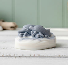 Load image into Gallery viewer, A handmade vegan soap featuring two grey dolphins jumping through white frothy waves; the base is white, and the dolphins are highly detailed, displayed on a light wooden surface against a soft farmhouse background.
