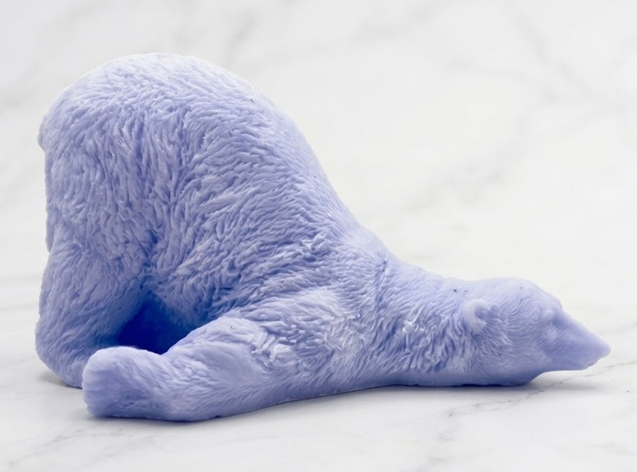 A soft blue bar of soap sculpted into a lazy polar bear figure lying down on its side, set against a white marble background.