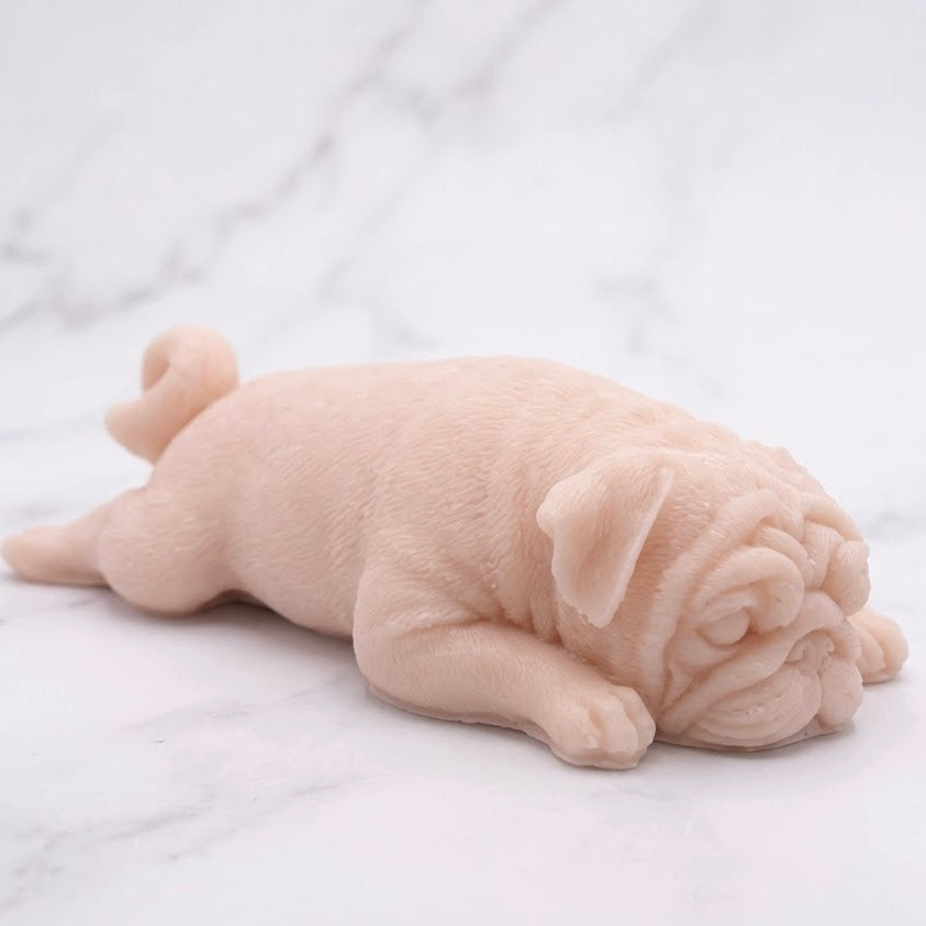 A soft pink pug-shaped vegan soap gift. resting on a light marble surface with a soft background.