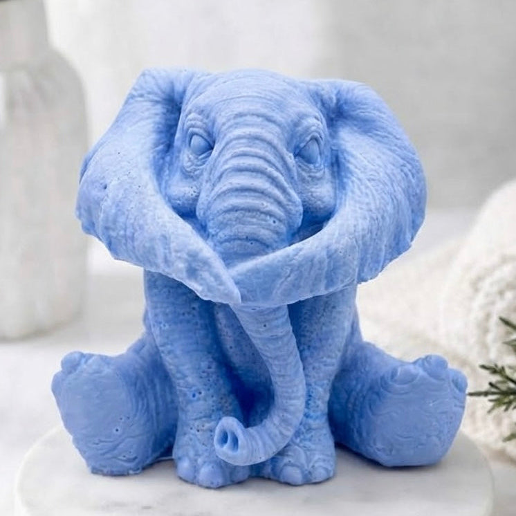 A light blue elephant vegan soap gift sitting on a white marble round pedestal, with a soft-focus neutral background and decorative props.