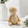 This soft yellow voodoo doll soap is highly detailed, including spiral eyes, a stitched mouth, and carved heart and belly patches, against a bright, softly blurred bathroom background