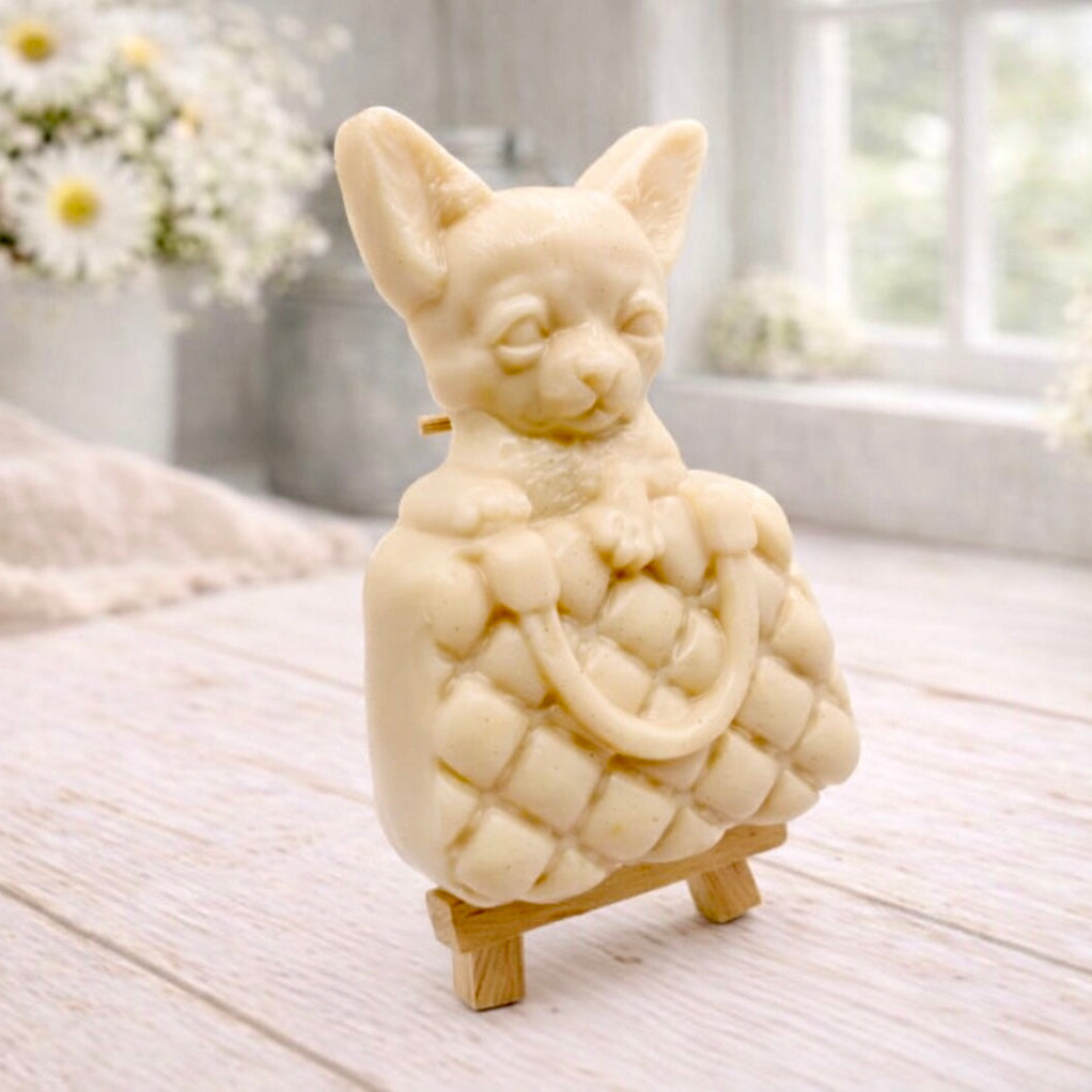 A highly detailed handmade vegan soap in a speckled grey marble finish, sculpted as a small chihuahua puppy with large ears peeking out from inside a quilted designer-style handbag, displayed on a miniature wooden easel.