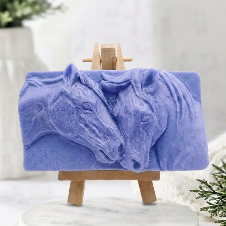 A lavender-blue coloured vegan and cruelty-free handmade soap bar with a highly detailed, sculpted relief carving of a mare and foal horses nuzzling. Natural bath and body product, detailed animal art soap.