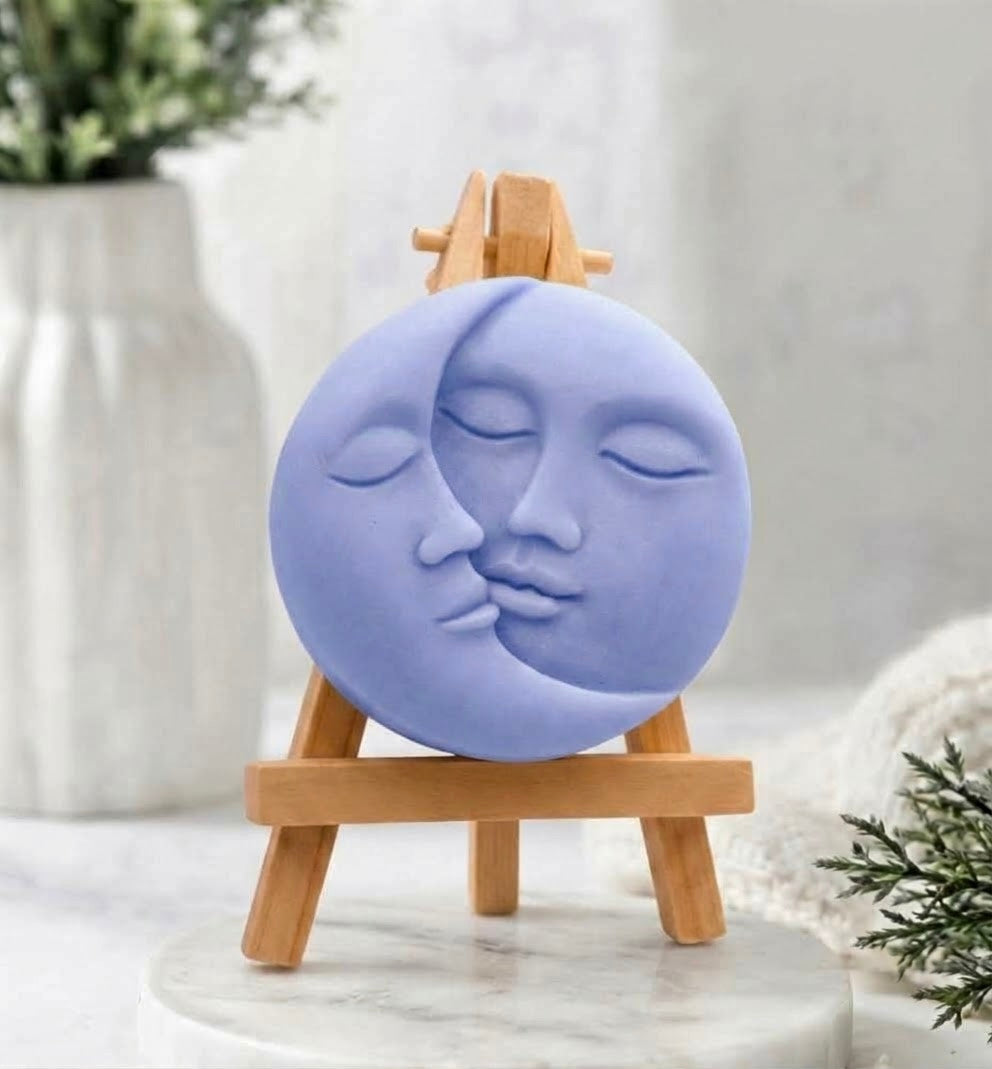 A soft-blue, round vegan soap with a detailed sun and moon kissing face design.