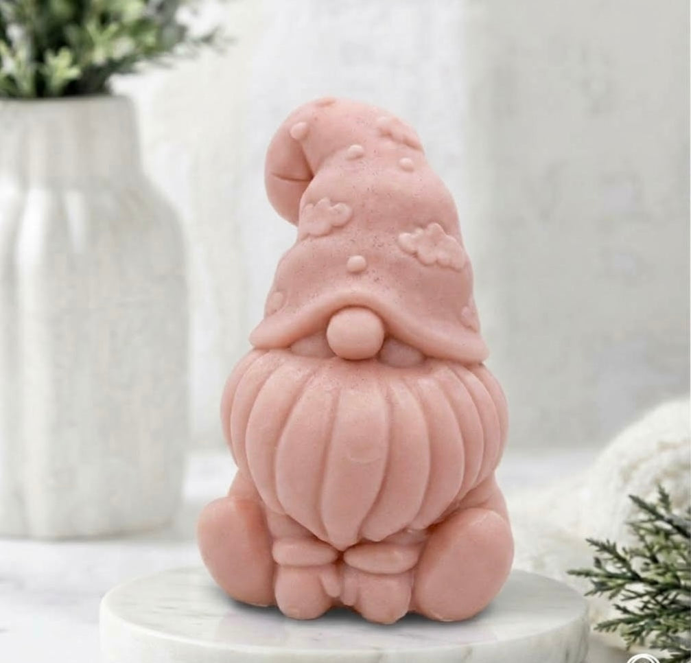A handmade vegan soap in a soft pink  tone, sculpted as a gnome (gonk) with a tall, curved hat that covers the eyes and has clouds on it, a round nose, and a long, textured beard.