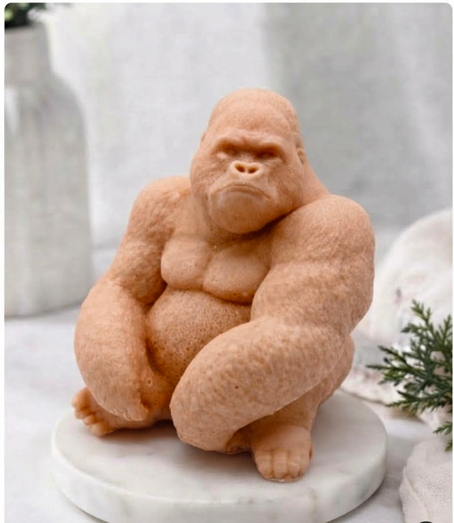 A large gorilla vegan soap in a seated pose on a round white marble base, photographed in a softly styled indoor setting with blurred decor in the background.