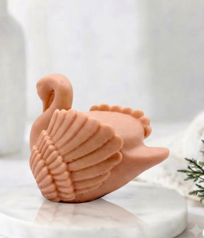 A side view of a handmade swan soap bar displaying detailed feather textures on a round display tray.