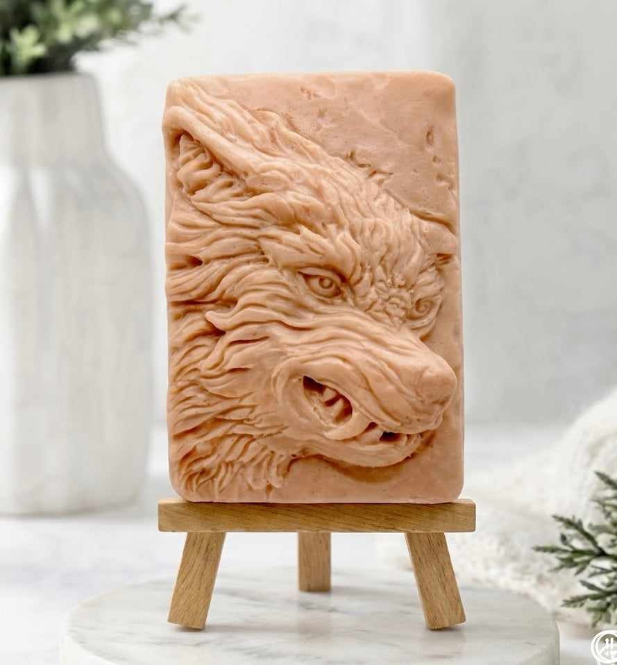 A rectangular red French clay soap bar featuring a highly detailed, raised relief carving of a wolf's head, displayed on a small wooden easel stand.