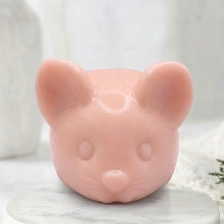 A front view of a soft pink handmade vegan soap sculpted into the shape of a cute resting mouse with large rounded ears and a delicate snout