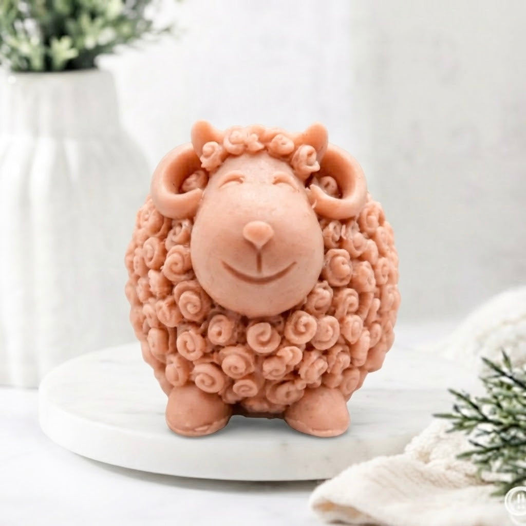 A terracotta sheep / Ram soap with curly textured wool, closed eyes, and a smiling face, displayed on a white surface against a soft blurred background.