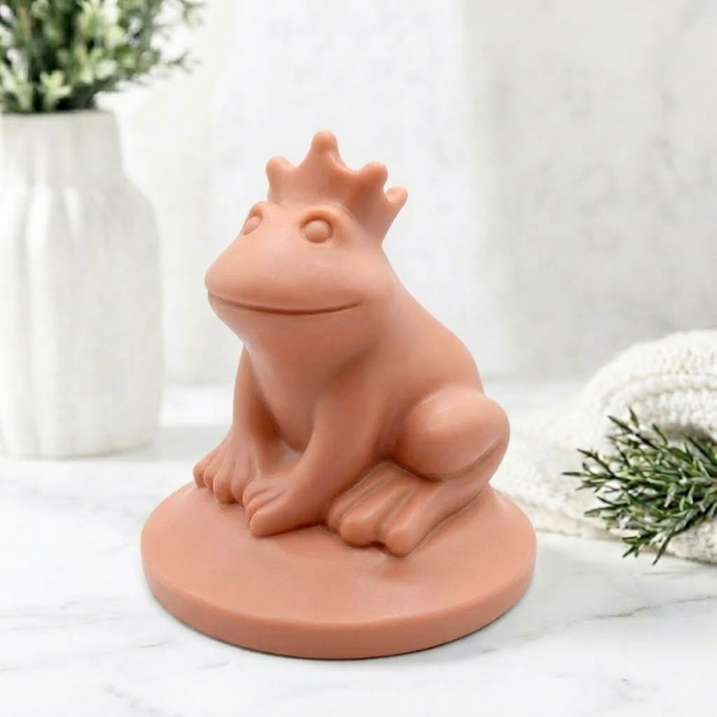 A side view of a terracotta coloured handmade vegan soap featuring a frog prince with a crown on his head, displayed on a white background