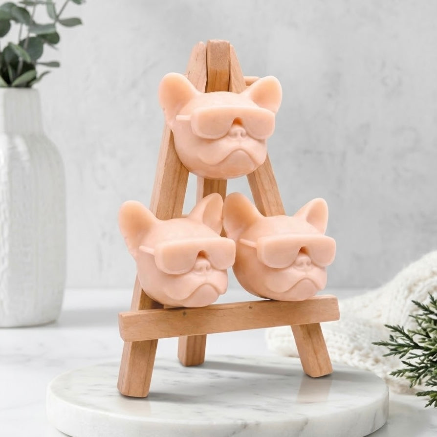 Artisan Frenchie novelty soap gift set, featuring three pale pink dog-shaped soaps in sunglasses stacked on a wooden easel display stand. Handcrafted gift for French Bulldog lovers.