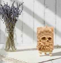 Load image into Gallery viewer, A handmade vegan soap featuring a highly detailed 3D relief of a skull wearing a jewelled crown and surrounded by roses, displayed on a wooden easel against a whimsical background.
