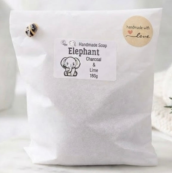 A white paper bag of handmade soap labeled 'Elephant' with charcoal and lime scent, featuring a small elephant illustration and a round 'handmade with love' badge.