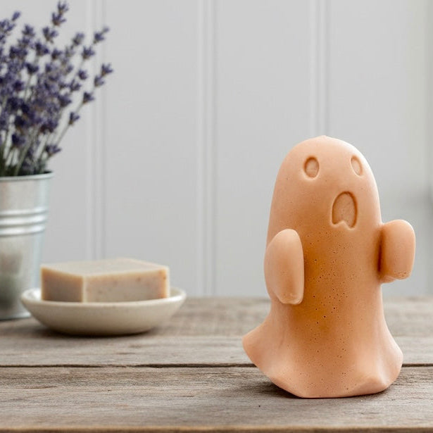 Ghost-shaped soap on a wooden surface with a plant and soap dish in the background.